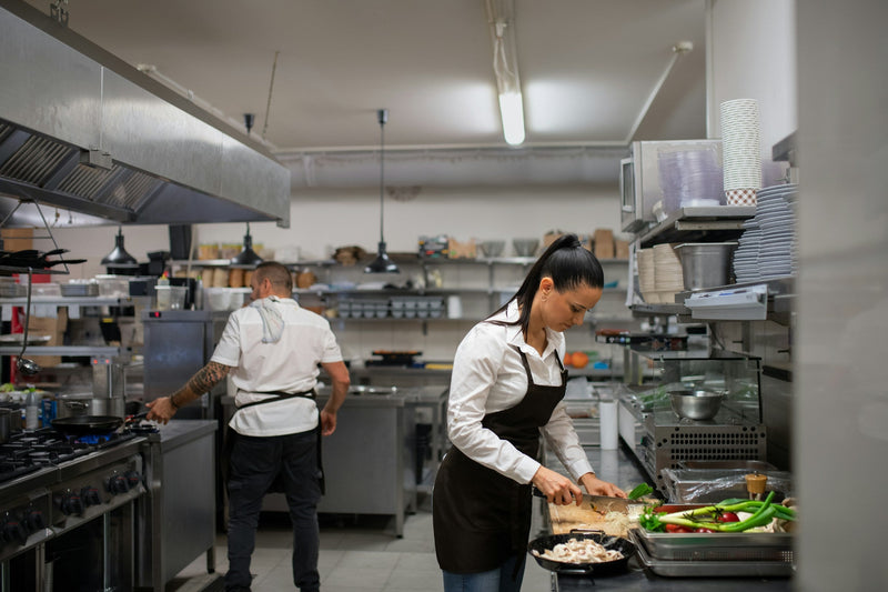Chef preparing food in a clean, well-equipped commercial kitchen with open shelving and stainless steel counters