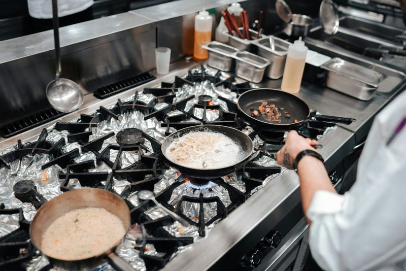 Overhead view of a professional kitchen stove with pans and sauces being prepared in a commercial setting