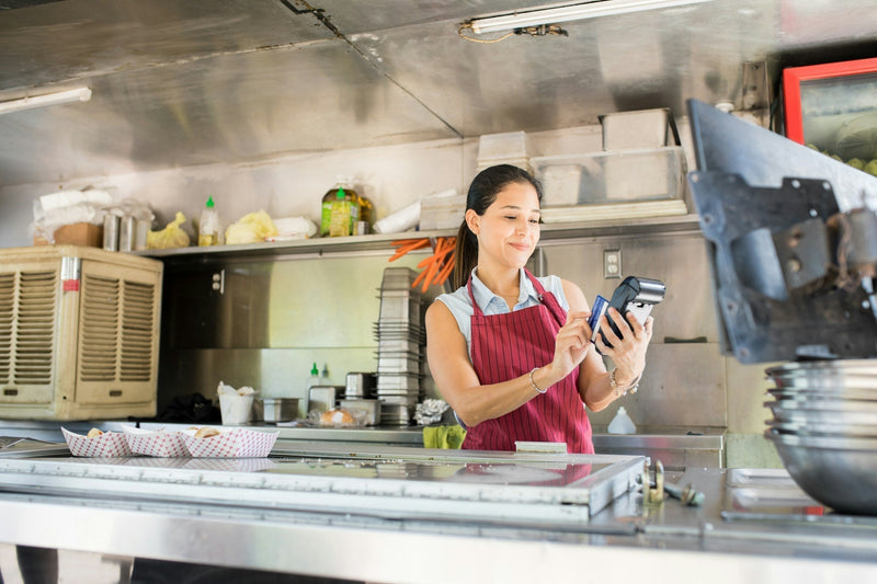 A food truck operator reviewing paperwork and operating equipment, symbolizing the regulatory aspect of running a mobile food business.