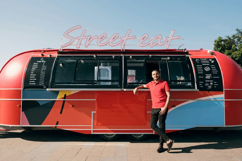 A food truck vendor standing outside a red and black food truck, ready to serve customers
