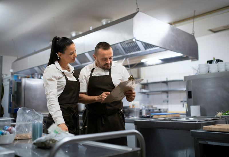 Two chefs in a ghost kitchen reviewing orders in a commercial kitchen setup