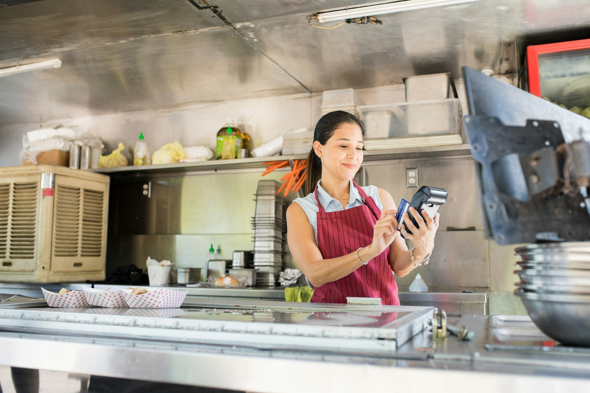 A food truck operator reviewing paperwork and operating equipment, symbolizing the regulatory aspect of running a mobile food business.
