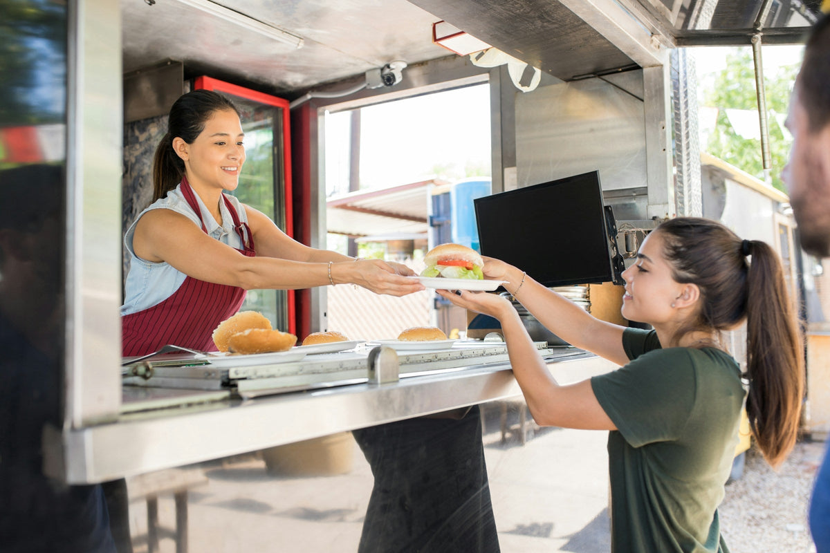 Two food truck workers serving customers through the truck’s window, highlighting the dynamic nature of the food truck business.