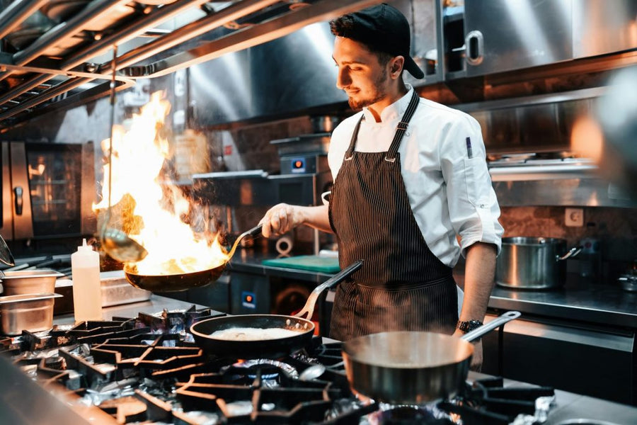 Chef flambéing food in a ghost kitchen with stainless steel equipment and modern appliances