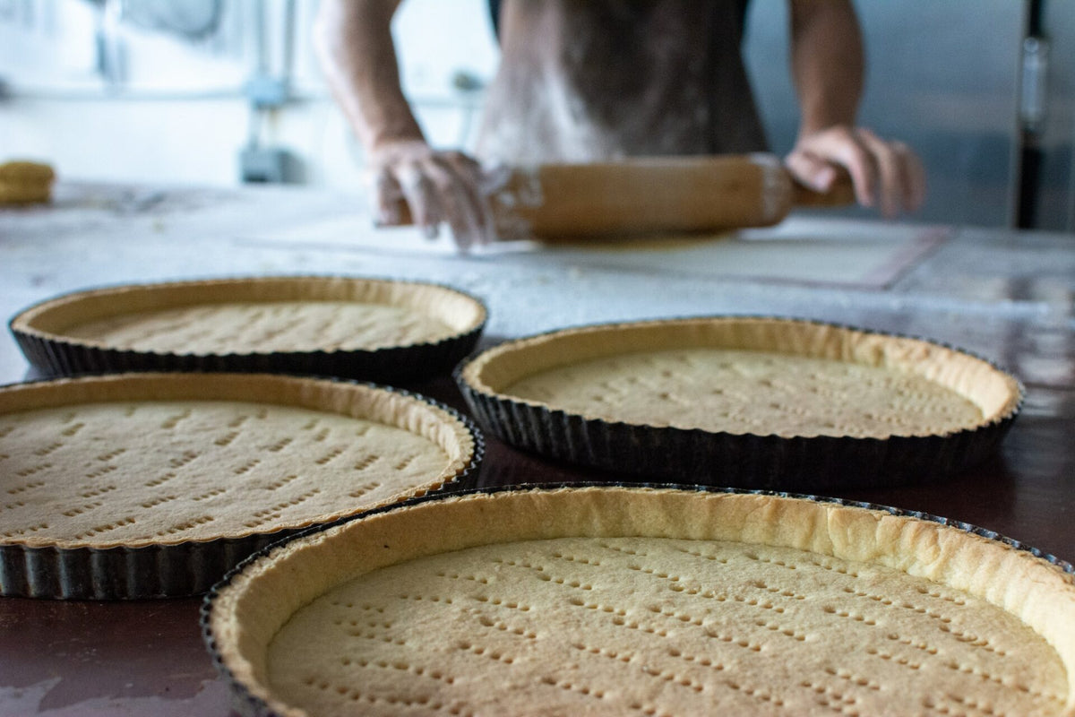 Pre-baked tart shells on a worktable with a rolling pin in the background.