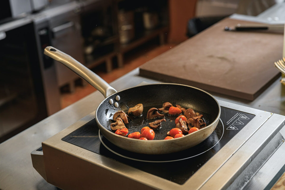 Cherry tomatoes and mushrooms being sautéed on a hot pan over an induction stove

